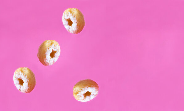 Homemade donut with powdered sugar in motion falling on the pink background. Copy space.