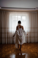 A girl in a white silk dressing gown near the window. Bride in a bathrobe near the window