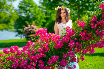 Spring sexy fantasy woman enjoys standing near flowering pink roses. Outdoor portrait of young beautiful happy smiling lady posing. Youth, romantic and lifestyle concept. Copy, empty space for text