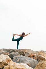 Beautiful woman standing in Natarajasana exercise, Lord of the Dance yoga pose (Lord Shiva’s) on a beach rock. Full length of sportive lady, working out. Relaxing and Mental health concept. Copy space