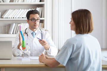 Male doctor orthopedist explaining to his female patient with serious injury and back ache