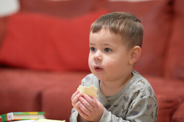 expressive young boy eating cheese at home while watching tv next to the couch