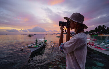 Photography and travel. Young woman in hat holding camera with beautiful tropical sea view.