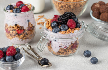 Chocolate granola with berries, chia seeds and natural yogurt in two jars on light gray background