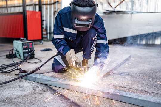 Welding, male worker welding metal workpiece outside factory, protective clothing protective gloves and safety helmet, welding sparks and light