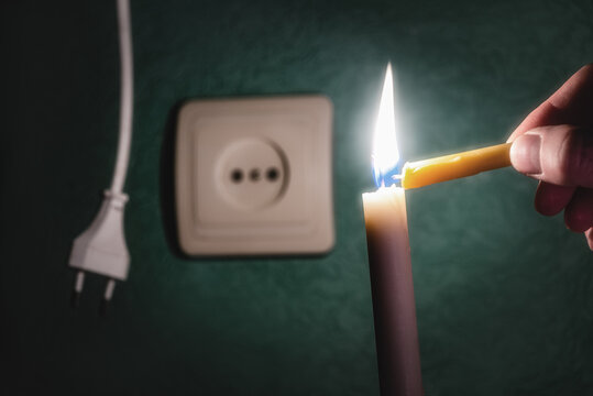 A burning candle next to an outlet and an electric plug. Blackout, power outage, energy crisis or power outages, conceptual image. Ukraine, the lack of light due to an accident at an electric power