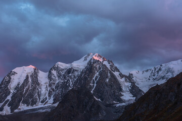 Awesome landscape with sunset pink reflection on huge snowy mountain top in violet dramatic sky. Hanging glacier and cornice on giant snow mountains in dusk. Snow-covered mountain range in twilight. © Daniil