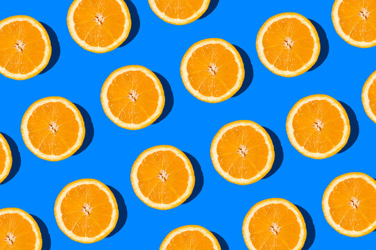 Summer flat lay pattern made with fresh orange fruit slices on vibrant blue background. Minimal sunlight concept with sharp shadows.