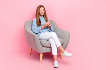 Fototapeta na wymiar Full body size photo of young teen age schoolgirl brown hair wear blue knitted pullover chatting online sit sofa isolated on pink color background