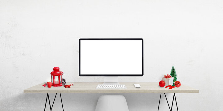 Blank computer display on work desk surrounded by Christmas decorations. Isolated screen for Christmas greeting text, web page or product presentation