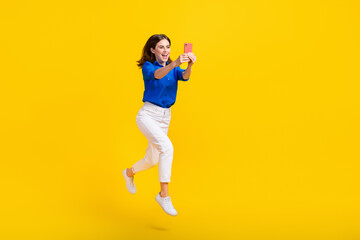 Full length photo of excited pretty lady wear blue shirt jumping high recording video vlog device isolated yellow color background