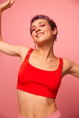 Fashion portrait of a woman with a short haircut of purple color and a smile with teeth in a red top on a pink background happiness
