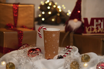 a cup of coffee or tea with a Christmas cozy design. Winter holiday decor, presents, fireplace with New Year golden light