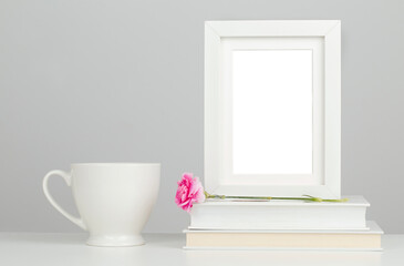 Fototapeta na wymiar White picture frame mockup on desk with books, porcelain mug and pink flower 