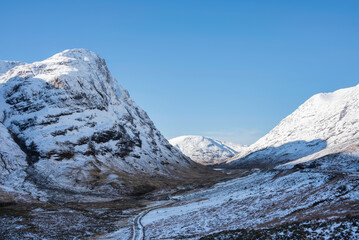 Gorgeous Winter landscape blue sky image of view along Glencoe Rannoch Moor valley with snow covered mountains all around