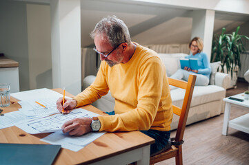 Senior man sitting at table and looking into blueprints of his new home