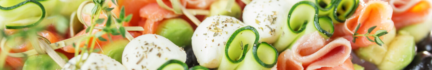 Appetizers with red fish, avocado, mozzarella and cucumbers close-up. Food and catering concept.