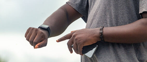 African black man pointing finger at smartphone, blank screen, with smartwatch, street lifestyle, blurred background