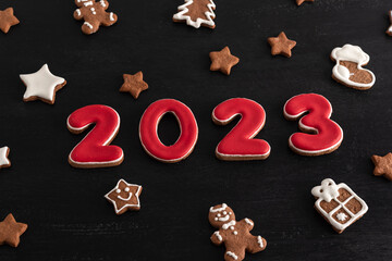 Inscription 2023 from gingerbread cookie. Christmas bacing, black background