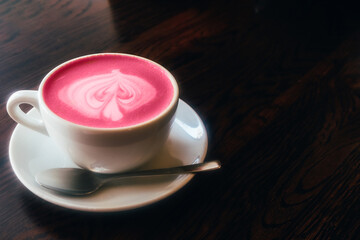 A cup of cappuccino with pink foam on a dark table.