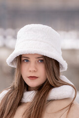 Close up portrait of young woman in white fur panama and beige sheepskin coat in winter outdoors. Trendy youth outerwear