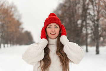 Pretty girl in wool red hat and mittens smiles right into camera. Woman in knitted clothes in winter forest