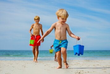 Little boy run holding bucket on sand beach with friend