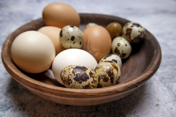 fresh quail and chicken eggs from the farm in a brown clay plate on a gray marble table. selective soft focus. High quality photo