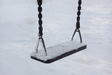 empty swing on playground in winter with snow