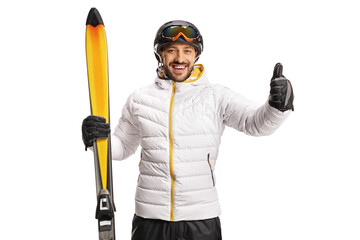 Cheerful male skier holding skiis and showing thumbs up