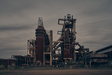 Old German blast furnace factory from the old industry in a dark color grading. There is an...