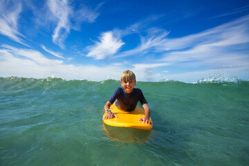 Cute boy swim on surf board smiling and looking at camera