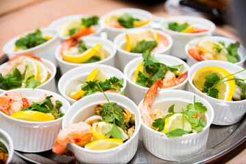 Many servings of seafood with lemon in ramekins, shrimp, mussels and squid rings garnished with cilantro leaves