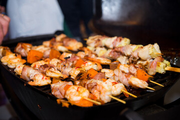 Shashlik (shish kebab) on skewers is cooking on grill. Slices of yams (sweet potatoes), bacon.