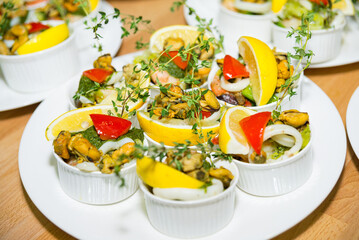 Mussels with a slice of lemon and microgreens, squid rings and pesto sauce in ramekins, many servings