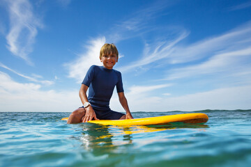 Cute young boy sit on orange surfboard in ocean