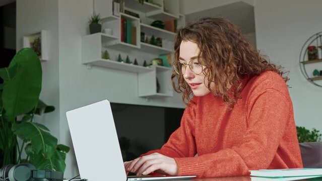 Young smiling pretty woman student using mobile phone and laptop modern technology, checking cellphone while remote working online or e learning from home sitting at table with computer.