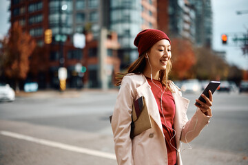 Young Asian woman choosing music on mobile app while walking in city.