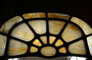 Goldgelb-wei&szlig;-braunes Rundbogenvordach aus Glas mit Mosaikmuster und Licht vor schwarzem Himmel bei Nacht im Winter