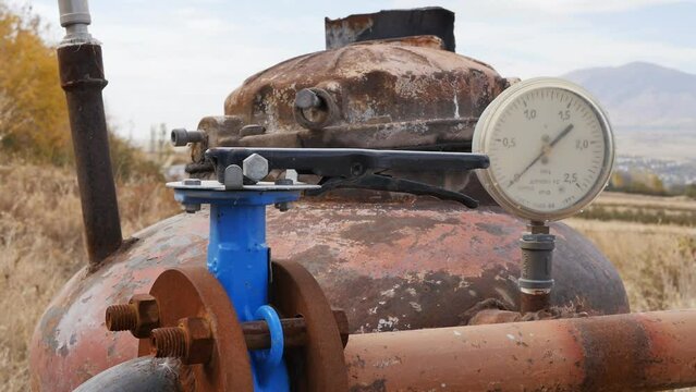 A close-up of an outdated pumping station for pumping water from underground to irrigate fields with agricultural crops. A rusty well consists of a tank, a valve and a water pressure gauge.
