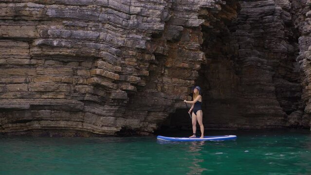 Young woman is paddling on a sup board among beautiful rocks