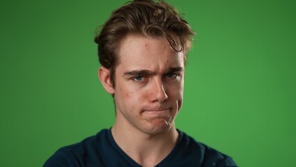 Closeup slow motion portrait of angry, upset, frustrated, young man 20s isolated on green screen color background in studio. Sincere emotions lifestyle concept