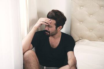 Negative upset serious beard man sadness stress headache problem sitting beside bed in apartment....