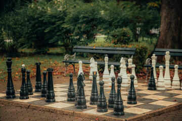 King size standing chess outside in a park. Black and white playing figures standing randomly on the checker board.
