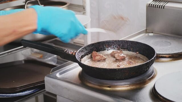 Grilled chicken liver in hot pan close up. Professional cook in blue gloves stirs and take off meat with iron kitchen spatula. Cooking, prepare ingredients for health and diet food delivery
