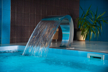 a modern large indoor pool with blue lighting and a waterfall.