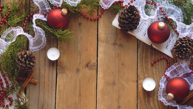 Christmas Flatlay of Pine Cones, Red Ornaments, Beads, Sheet Music, Candles, and Evergreen Boughs on a Wooden Background | Rustic Christmas Decorations