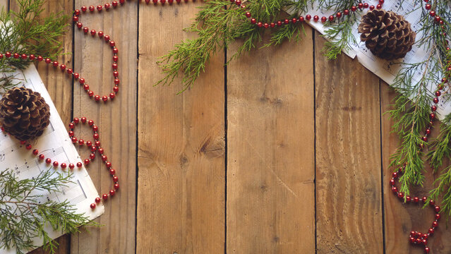 Christmas Flatlay of Pine Cones, Red Ornaments, Beads, Sheet Music, and Evergreen Boughs on a Wooden Background | Rustic Christmas Decorations