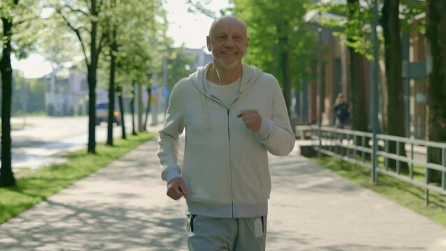 Mature smiled runner is running through the street listening to music while training. Sport and healthy lifestyle concept