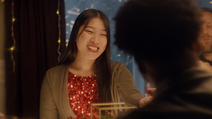 Asian woman drinks wine, talks and smile. Multi cultural friends celebrating Christmas or New Year 2023. Served holiday table. Warm atmosphere of Christmas dinner at home. Christmas party.